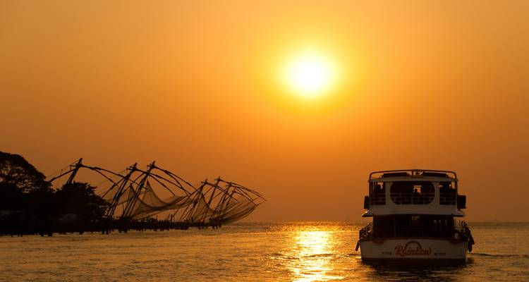 Chinesische Fischernetze als Silhouetten vor einem Sonnenuntergang am Wasser.
