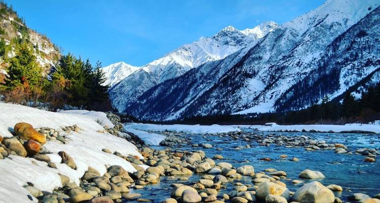 Rivier en met sneeuw bedekte bergen onder een heldere blauwe hemel.