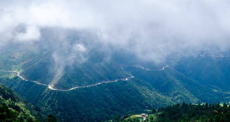 Ein malerischer Blick auf neblige Berge mit sich schlängelnden Straßen darunter.