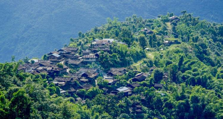 Ein Dorf, eingebettet zwischen grünen Hügeln, umgeben von dichter Vegetation.