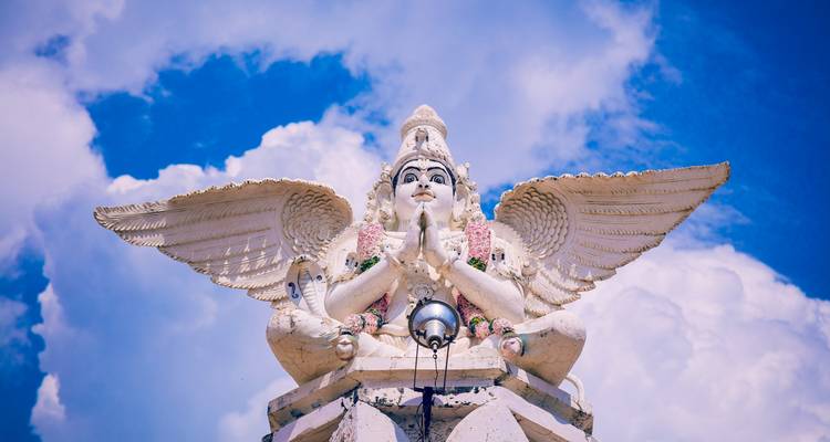 Statue of a winged deity with a bright blue sky background.