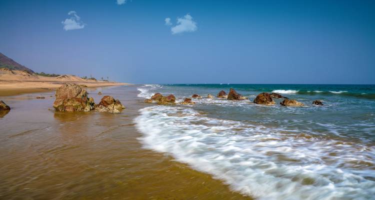 Küstenlandschaft mit felsigem Strand und Wellen, die an das Ufer schlagen.