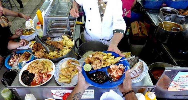 Étal de nourriture sur un marché animé où un chef distribue des assiettes garnies de fruits de mer frits, de frites et de quartiers de citron vert