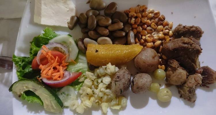 Plat équatorien traditionnel composé de maïs, fèves, avocat, viande rôtie et légumes racines sur un plateau blanc