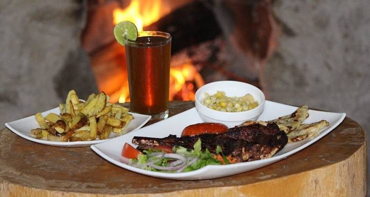 Viande grillée avec accompagnements et une boisson servie sur une planche en bois devant une cheminée crépitante