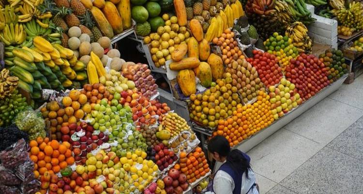 Éventail vibrant de fruits empilés en hauteur dans un marché couvert avec un vendeur sélectionnant des produits