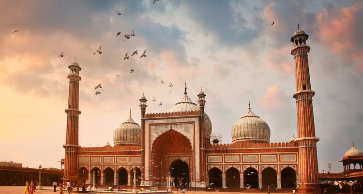 Jama Masjid bij zonsondergang met vogels die in de lucht vliegen.