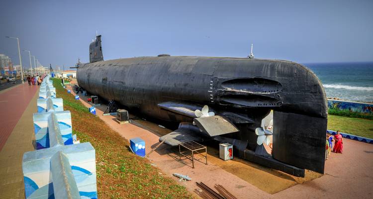Large submarine displayed on land near a promenade.