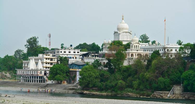 A riverbank with a white temple on a lush hill.