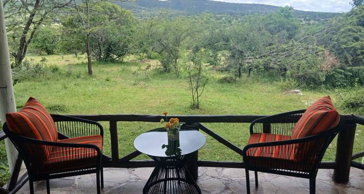 Veranda mit zwei gestreiften Sesseln mit Kissen und kleinem Tisch mit Blick auf die grüne Savanne.