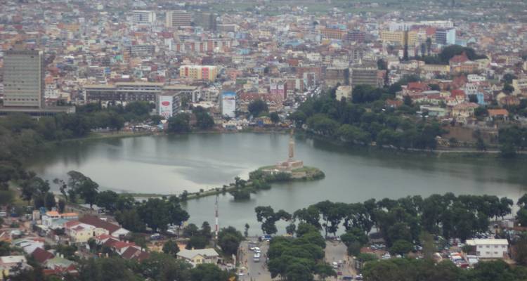 Panoramic city view with a lake in the foreground and buildings in the background.