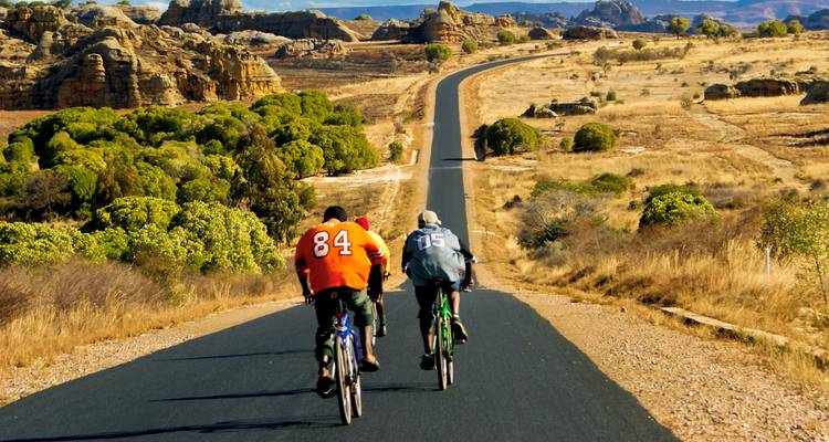Cyclistes sur une longue route au milieu d'un paysage aride.