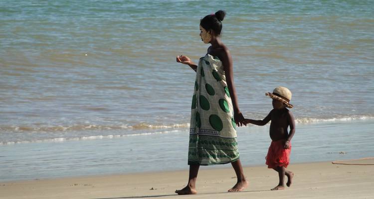 Femme et enfant marchant le long de la plage avec des vagues en arrière-plan.