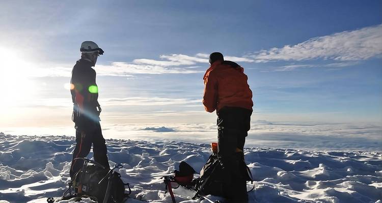 Des grimpeurs se tiennent sur un sommet enneigé au-dessus d'une mer de nuages avec les rayons du soleil matinal sur le côté.