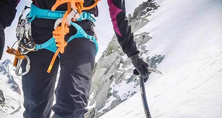 Bergsteiger mit Eispickel und Kletterausrüstung beim Aufstieg eines verschneiten Hangs
