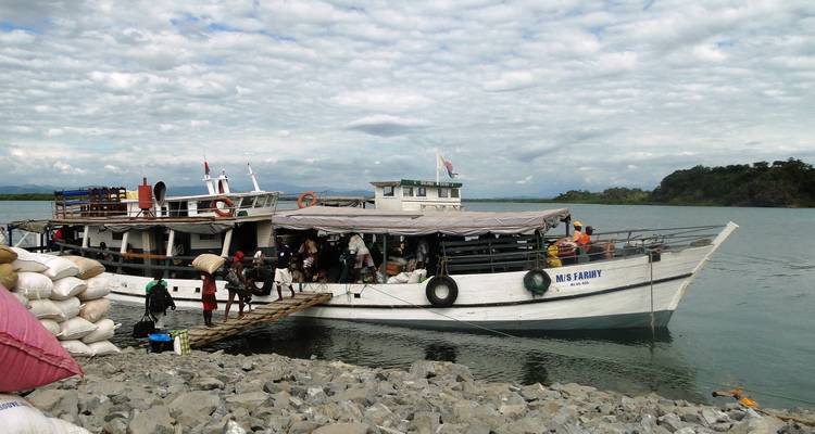 Large boat docked at rocky shore with people boarding.