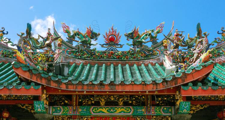 Las coloridas esculturas de dragones adornan el techo ornamentado con tejas verdes de un templo chino contra un cielo azul.