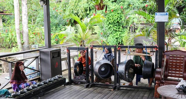 Los músicos locales con trajes tradicionales tocan gongs de bronce en una terraza de madera rodeada de plantas tropicales.
