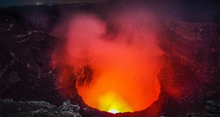 Un cráter de volcán humeante que emite un resplandor naranja brillante.