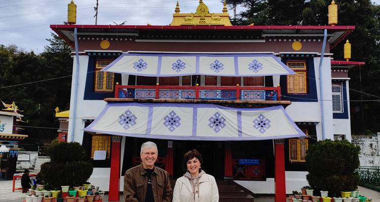 Two people standing in front of a Buddhist monastery with prayer flags.