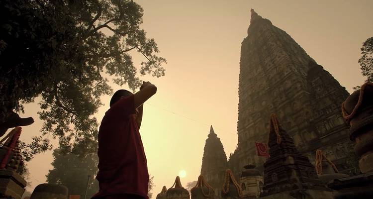 Visiteur en silhouette levant les mains devant l'imposant temple Mahabodhi dans la chaude lumière du crépuscule
