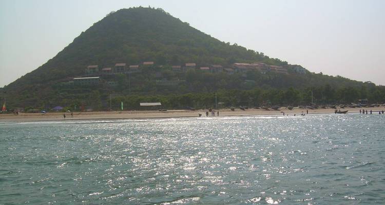 Mer scintillante de soleil avec une colline verte basse et des toits épars sur le littoral