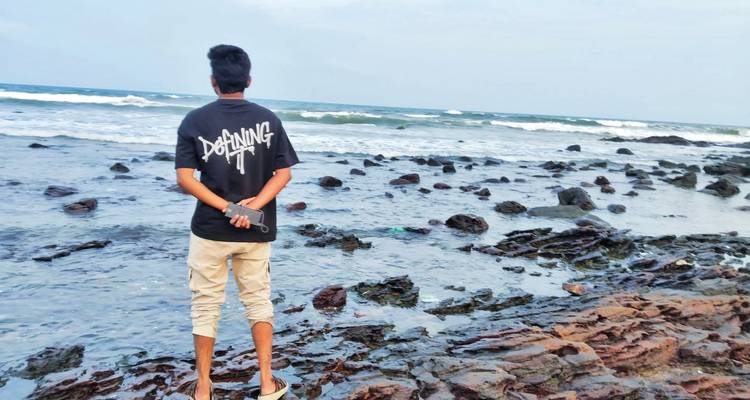 Jeune homme debout sur la rive rocheuse regardant la mer agitée par temps nuageux