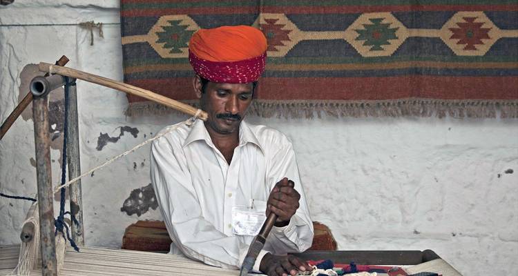 Man die stof weeft op een traditioneel weefgetouw met kleurrijke patronen.