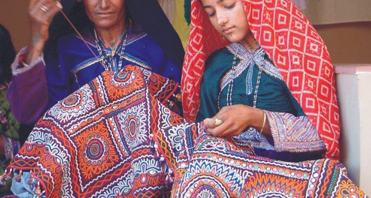 Zwei Frauen in traditioneller Kleidung arbeiten an einem bestickten Textil.