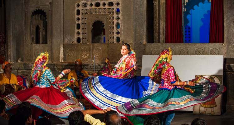 Vrouwen in kleurrijke traditionele klederdracht die binnenshuis dansen.