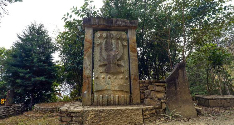 Stone monument with symbolic carvings in a forested area.