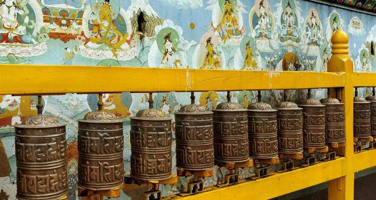 Rij gebedsmolens tegen een religieuze muurschildering.