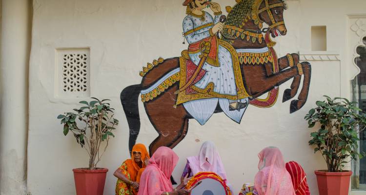 Vrouwen in traditionele kleding met een muurschildering van een man op een paard.