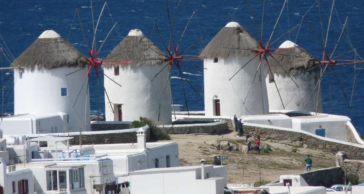Molinos de viento icónicos en una colina en Mykonos con gente cerca.