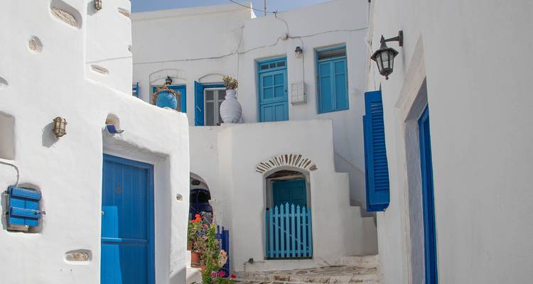 Callejón estrecho con puertas y ventanas azules en un pueblo griego.