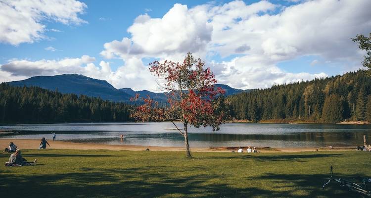 Personas relajándose junto a un lago pintoresco con árboles y montañas.