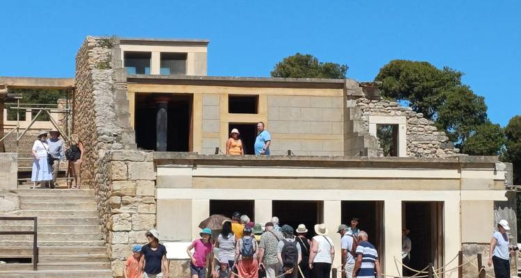 Visitors examining multi-level Minoan ruins at Knossos under clear blue sky.