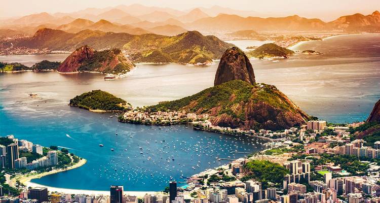 Iconic aerial view of Rio de Janeiro’s Sugarloaf Mountain surrounded by bays, beaches and city skyline at sunset glow.