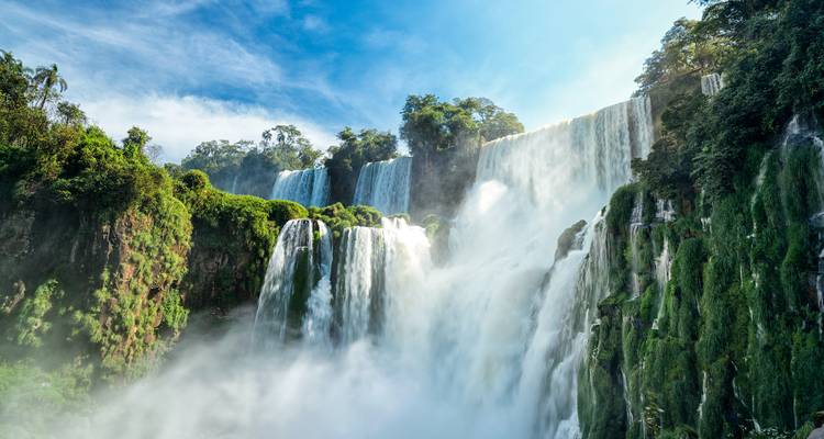 Dramatic Iguazu Falls plunging through lush subtropical jungle with mist rising into the sunlight.