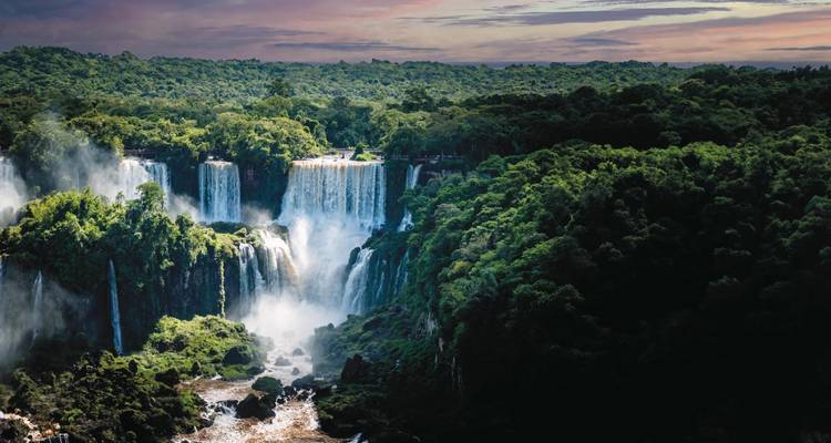 Powerful multi-tiered Iguazu Falls thunders through lush, dense rainforest at dusk.