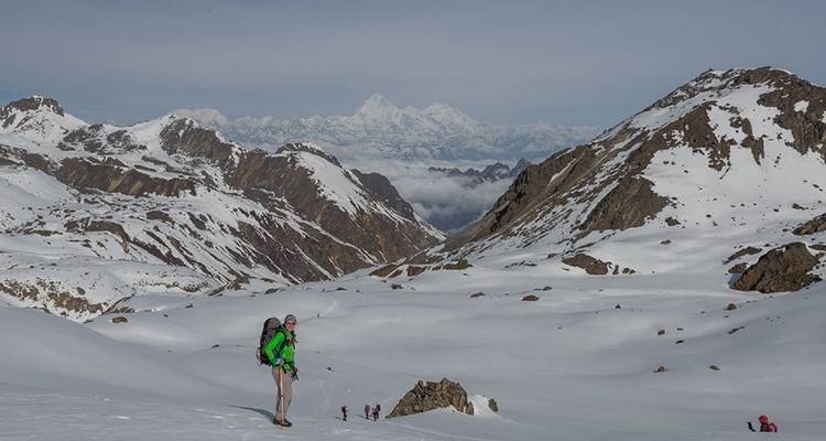 Wandelaar klimt door besneeuwd landschap met uitzicht op bergen in de verte.