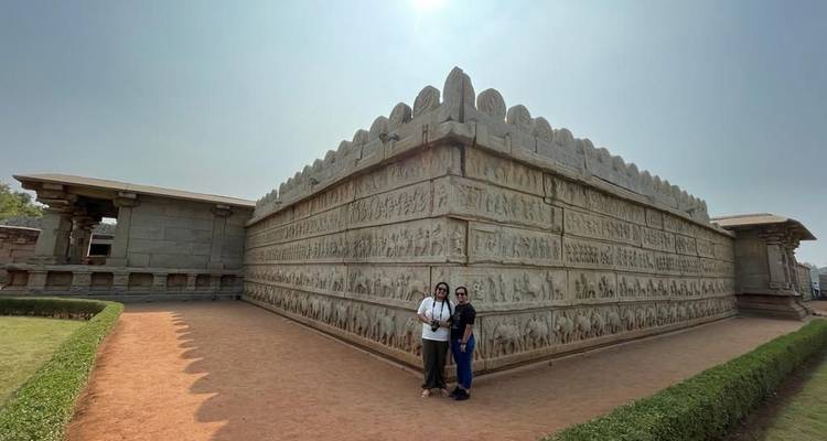 Twee mensen poseren voor een grote stenen muur met gravures.