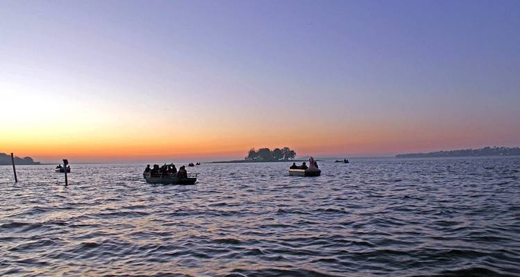 Mensen in boten die genieten van een meer tijdens zonsondergang.