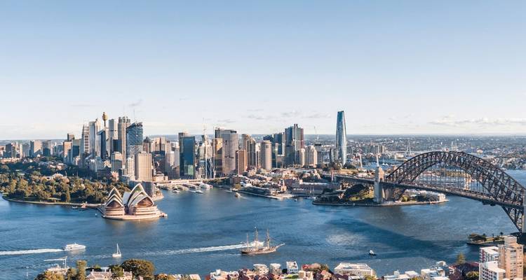 Vue panoramique aérienne du port de Sydney mettant en évidence l'Opéra de Sydney, le Pont du Harbour Bridge et l'horizon du centre-ville par une journée ensoleillée et dégagée.