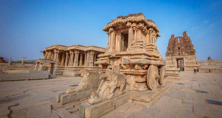 Steinerner Wagen und antike Ruinen unter blauem Himmel.
