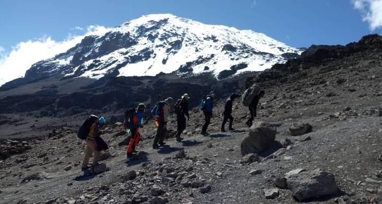 Randonneurs gravissant un sentier de montagne avec un sommet enneigé devant eux.