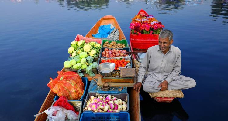 Un homme vendant des légumes et des fleurs sur un bateau dans un lac.