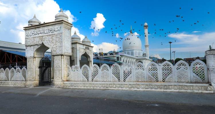 Une belle mosquée avec des sculptures blanches complexes et des oiseaux qui volent dans le ciel.