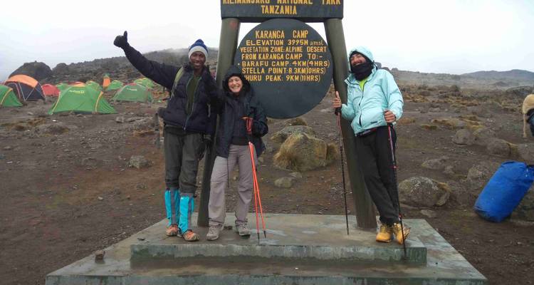 Tres personas posando en el letrero de elevación del Campamento Karanga.