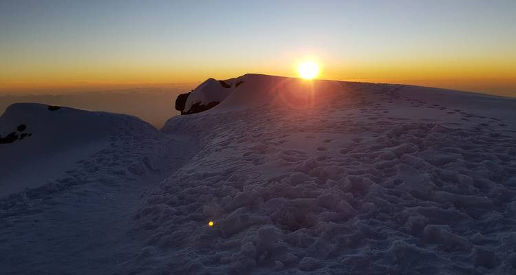 Sol saliendo sobre un paisaje montañoso nevado.